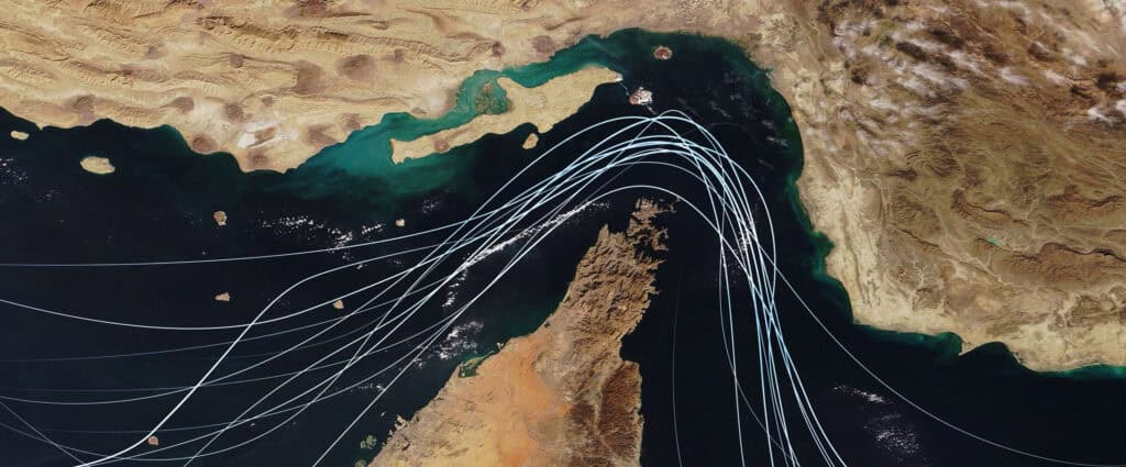 Satellite view of the Strait of Hormuz with white graphic lines representing global shipping lanes and maritime traffic between the Persian Gulf and Gulf of Oman Strategic oil transport concept