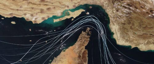 Satellite view of the Strait of Hormuz with white graphic lines representing global shipping lanes and maritime traffic between the Persian Gulf and Gulf of Oman Strategic oil transport concept
