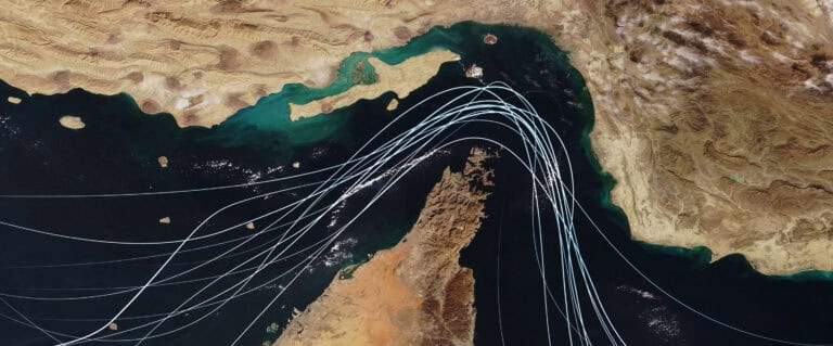 Satellite view of the Strait of Hormuz with white graphic lines representing global shipping lanes and maritime traffic between the Persian Gulf and Gulf of Oman Strategic oil transport concept